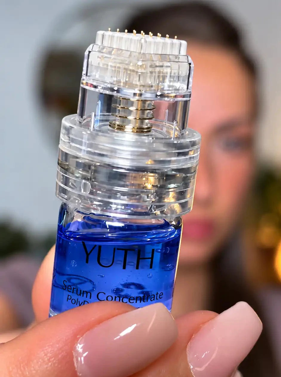 A close-up of a hand with manicured nails holding a small bottle of YUTH Serum Concentrate . The bottle is filled with a vibrant blue liquid copper peptide and has micro needles, with a blurred portrait of a woman in the background.